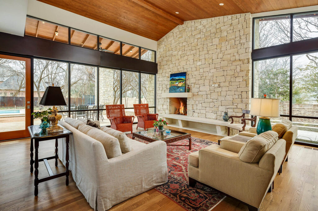 Luxury great room with wood ceiling, stone fireplace, and large windows in Dallas, T