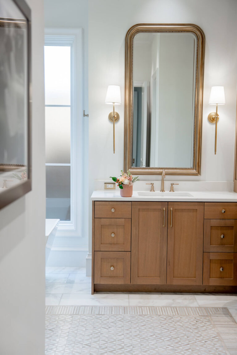 Brunswick primary vanity with framed mirror and brass sconces in transitional Dallas home